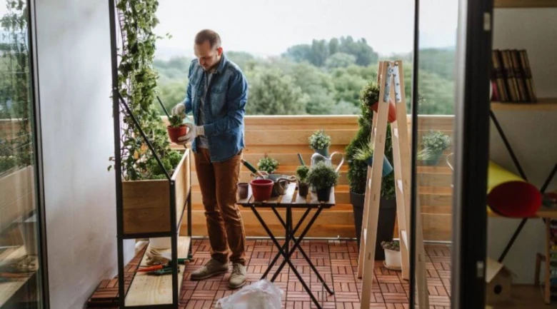 Muž se stará o rostliny na malém městském balkóně.