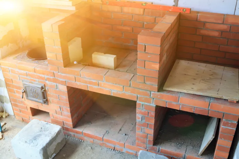 Částečně postavený kamenný krb z cihel s kovovým dveřmi