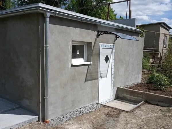Nově omítnutá malá stavba s bílými dveřmi v zahradním prostředí.