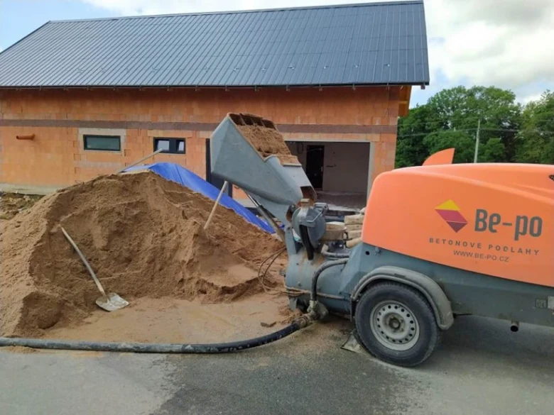 Stavební čerpadlo nalévá písek před nedokončenou budovou.