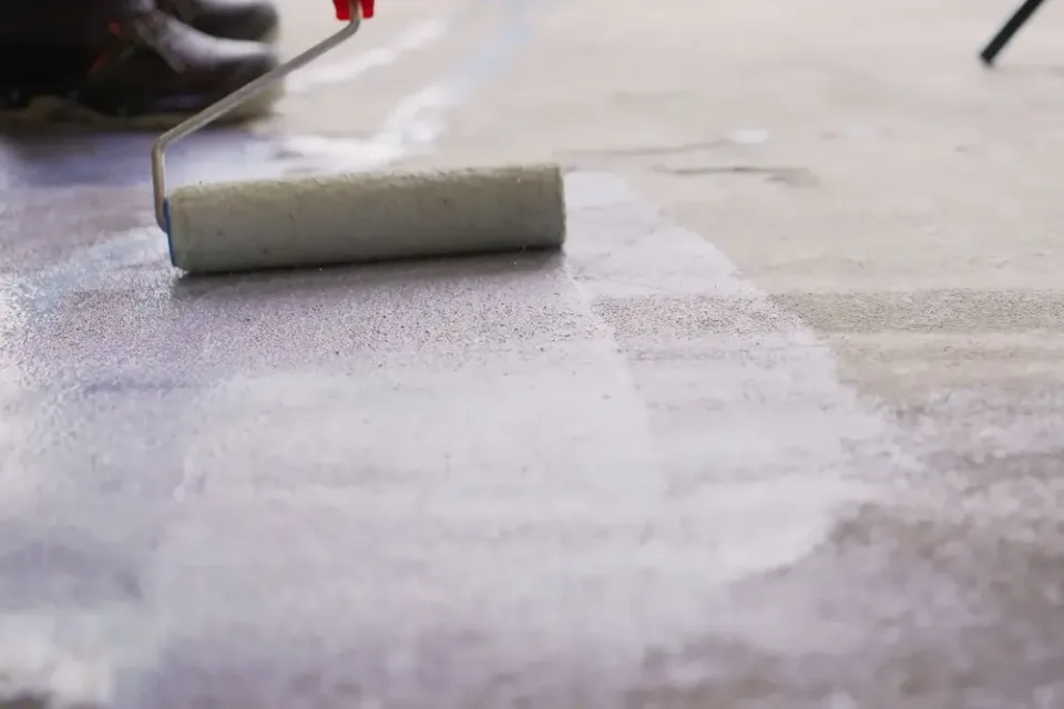 Nátěr betonu válcem s bílým penetračním nátěrem.