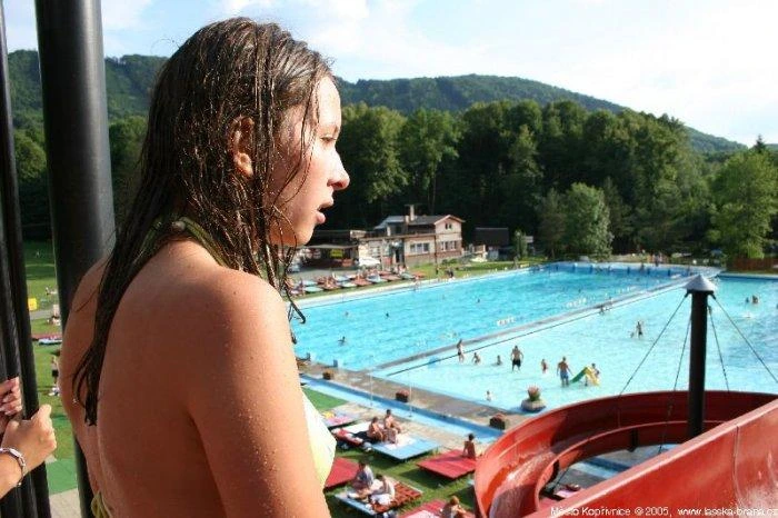 Dívka u bazénu v kopřivnickém koupališti s horami na pozadí.