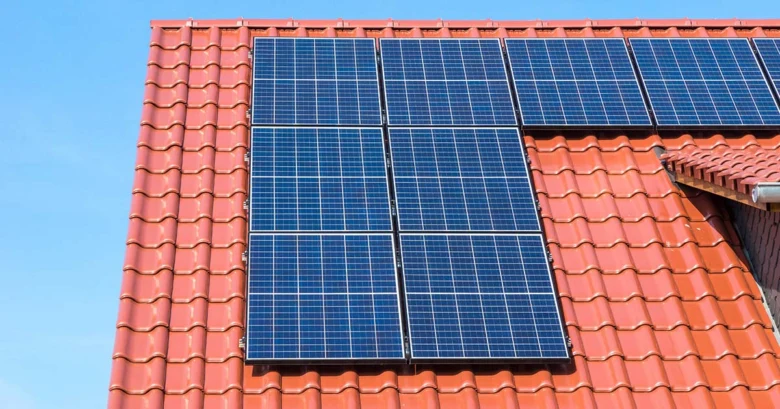 Fotografie modrých fotovoltaických panelů na červené střechě domu.