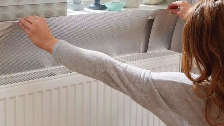 Žena aplikuje izolační folii na radiátor.