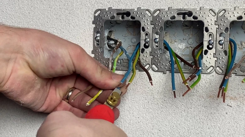 Ruční zapojení vypínače s viditelnými vodiči v elektrické krabici.