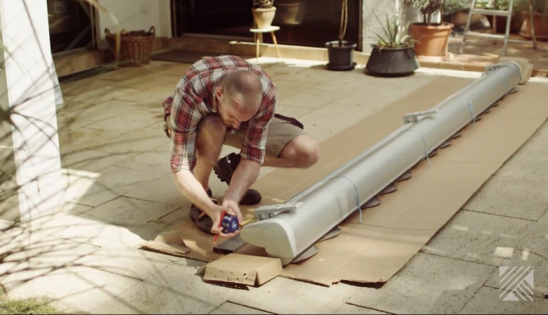 Muž měří bílou markýzu na balkoně při instalaci.