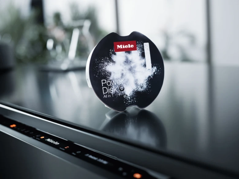 Tableta na myčku nádobí značky Miele stojící na ovládacím panelu.