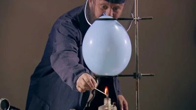 Muž nafukuje vodíkovou bublinu ohříváním plynu plamenem.