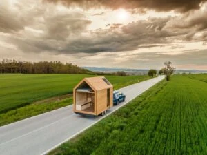 Malý dřevěný dům na přívěsku táhne auto po silnici.