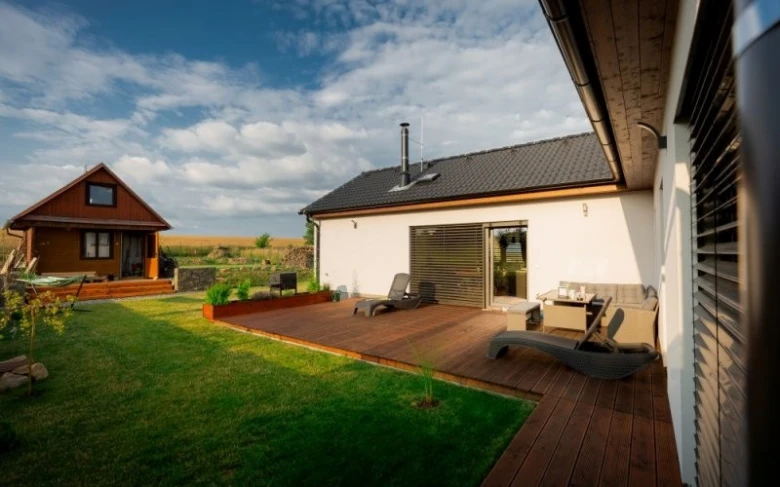Moderní dřevostavba bungalov s terasou na pozadí zelené trávníku.