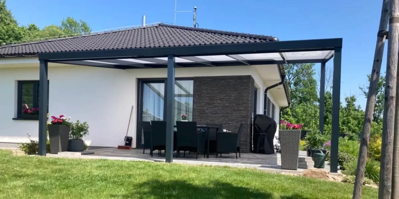 Moderní černá pergola nad zahradním posezením u domu.