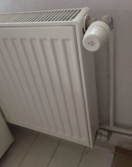 Bílý litinový radiátor s termostatem na zdi v interiéru.