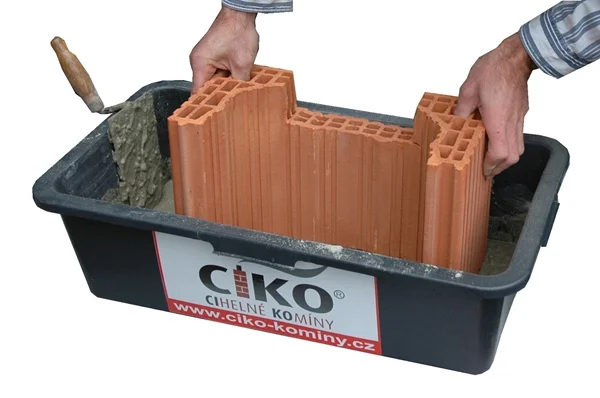 Ruční stavba cihlového komína v kontejneru s maltou.