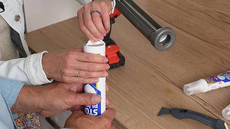 Ruce aplikují bílý silikon z pistole na dřevěný povrch.