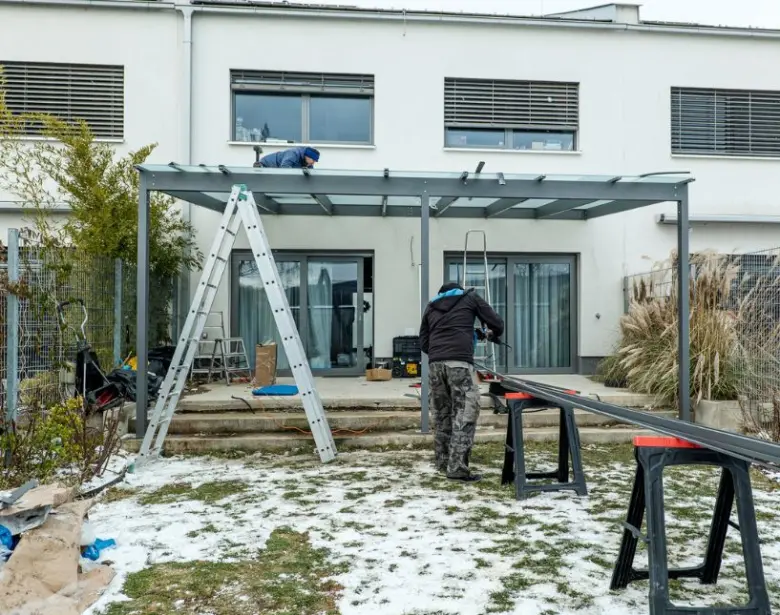 Dva lidé staví kovovou pergolu u domu v zimě.