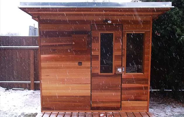 Venkovní dřevěná sauna v zimním prostředí s padajícím sněhem.