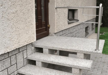 Betonové venkovní schody vedoucí k vchodu s kovovým zábradlím.