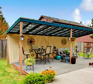 Pergola s tmavě zelenou střechou nad zahradním posezením.