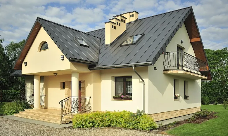 Moderní dům s tmavou plechovou střešní krytinou na pozadí zelené zahrady.