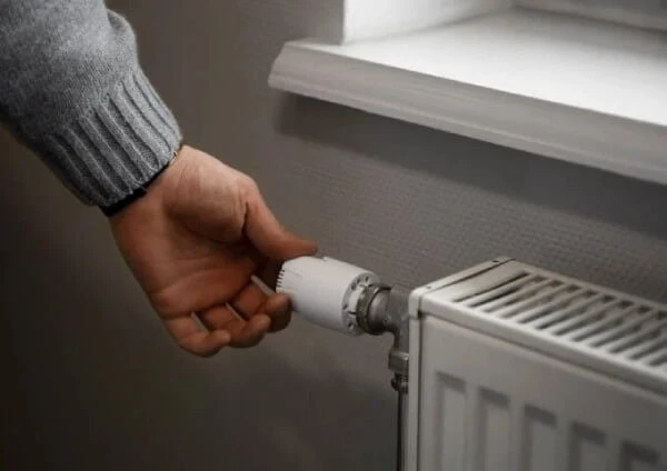 Ruka nastavuje termostat na radiátoru pro úsporu energie.