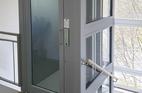 Moderní domácí výtah s ocelovými dveřmi a skleněnou stěnou.