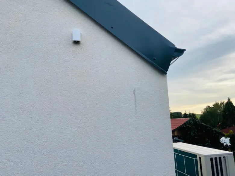 Bílá fasáda domu s tepelným čerpadlem venku.