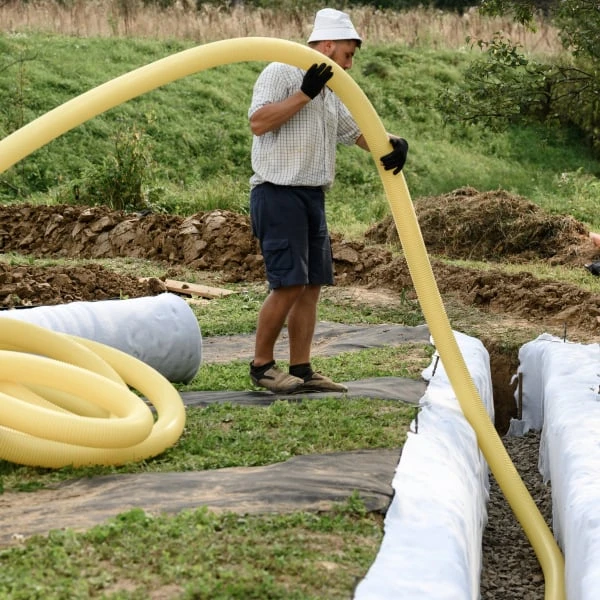 Muž instaluje žlutou hadici pro odvod dešťové vody do příkopu.