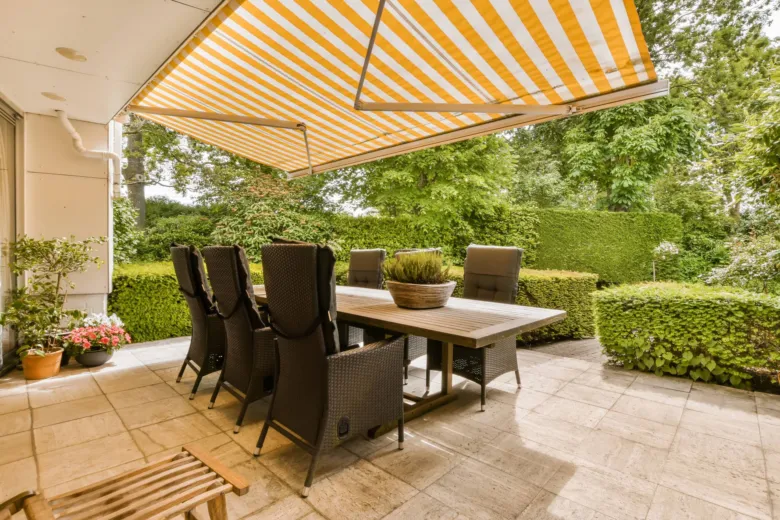 Žlutobílá markýza nad venkovním jídelním stolem na balkóně.