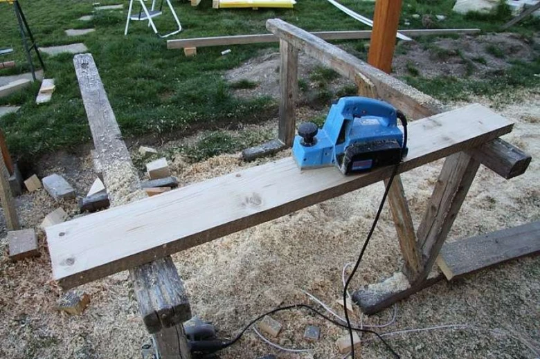 Modrý elektrický bruska na dřevěné prkno při stavbě houpačky.