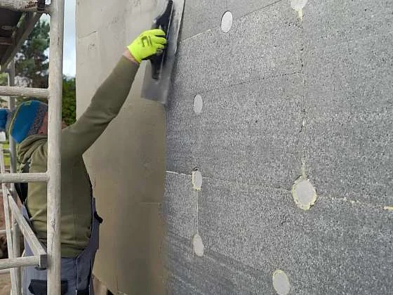 Stavebník nanáší lepidlo na fasádní desky pomocí stěrku.