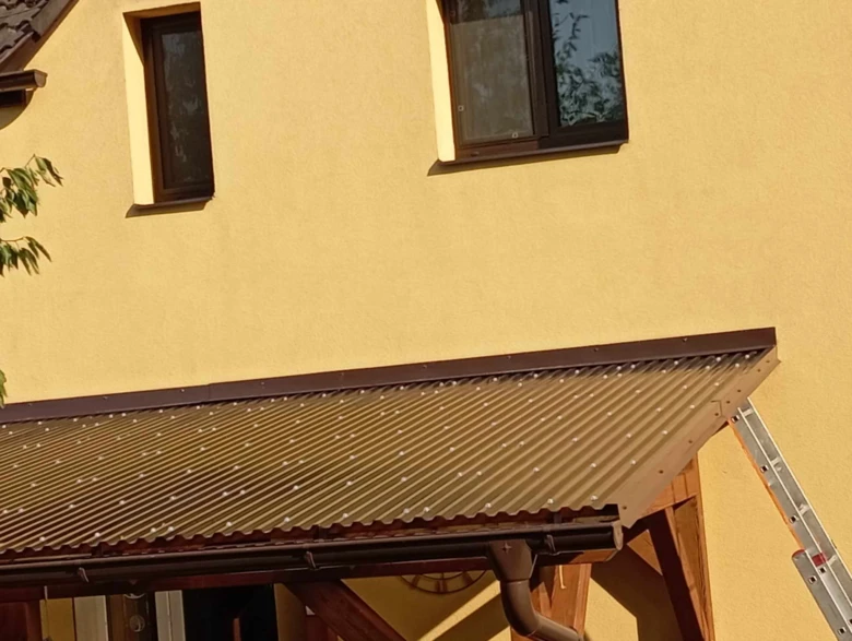 Montáž oplechování střechy s lištami na žluté fasádě domu