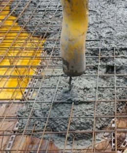 Zelený beton se nalévá přes železnou mřížku na staveništi.