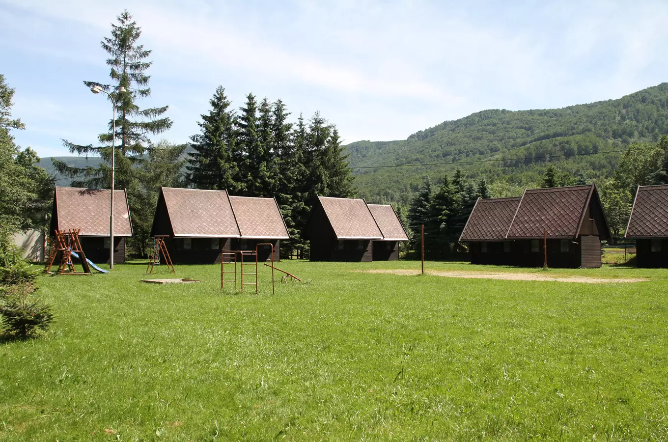 Kempování v Hejnicích: dřevěné chaty na trávníku s hory.