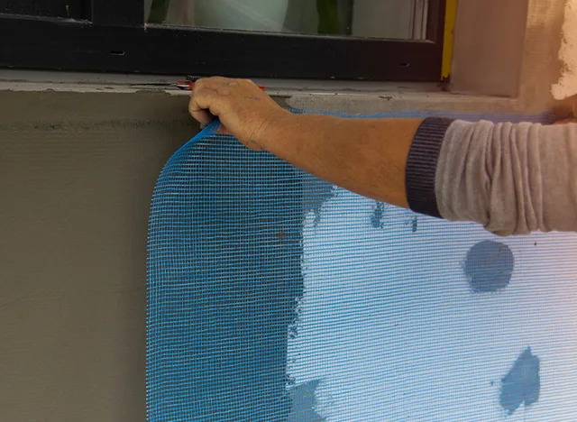 Ruka přitiskuje modrou perlinku na fasádu při práci s lepidlem.