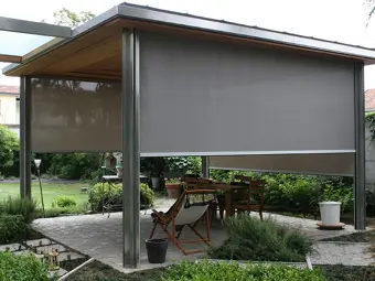 Moderní pergola s roletami poskytující stín pro venkovní jídelnu.