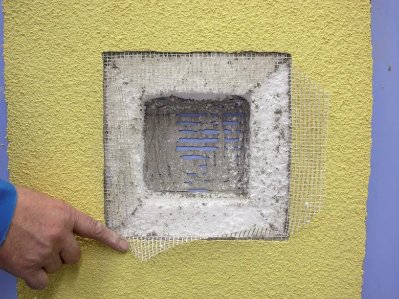 Detail opravy fasády s odhalenou mřížkou větracího otvoru.