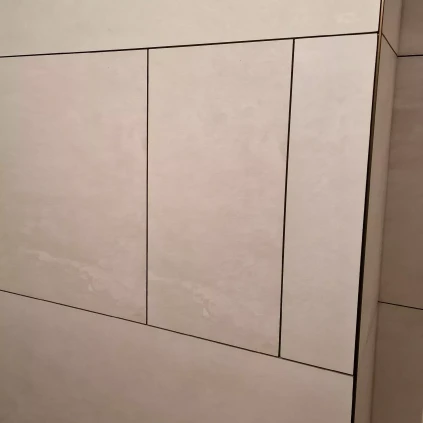 Bílá dlažba na zdi s tmavými spárkami pro revizní dvířka.