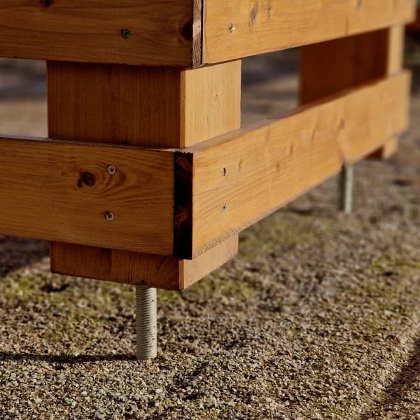Dřevěná pergola s kovovými kotvami na zemi.