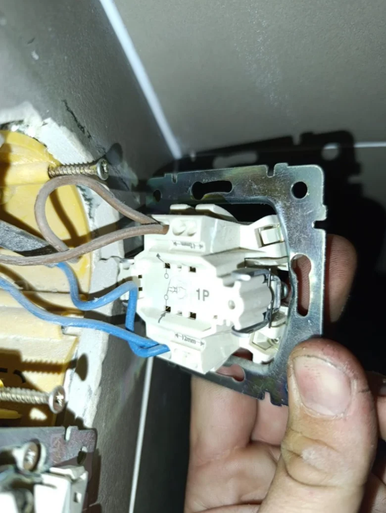 Instalace elektrického spínače s viditelnými vodiči v kovovém rámu.