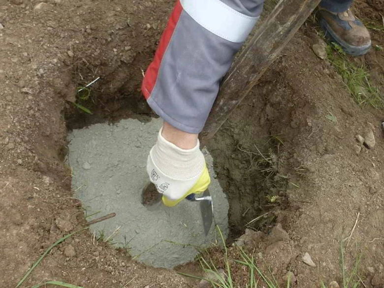 Pracovník nalévá rychle tvrdnoucí beton do vykopaného jámy.