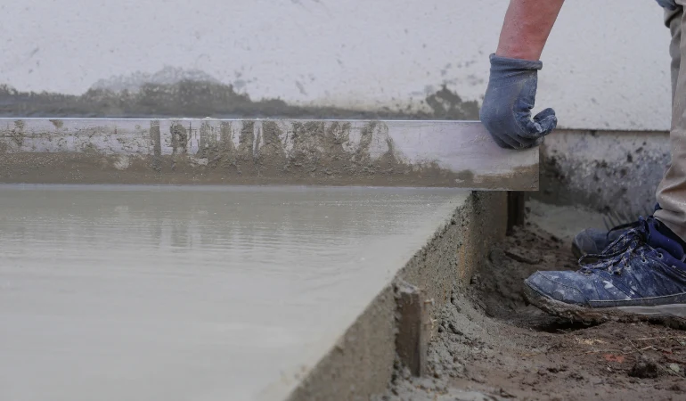 Stavebník vyrovnává čerstvý beton na terase pomocí pravítka.
