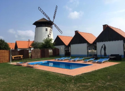 Koupaliště s lehátky před bílými chatami u větrného mlýna.