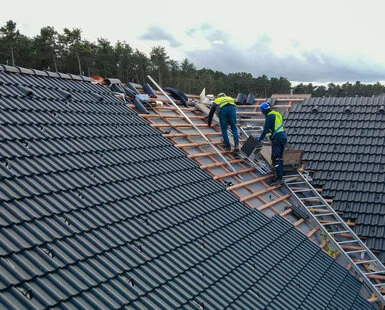Stavebníci montují dřevěný krov na střechu s taškami.