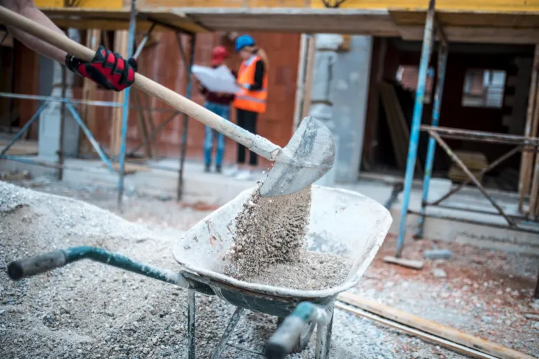 Stavebník překládá beton do vozíku na stavbě.
