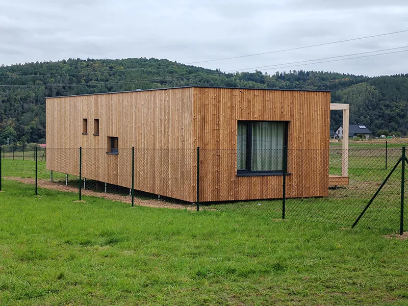 Moderní dřevěný modulární dům na trávníku s lesnatým pozadím.