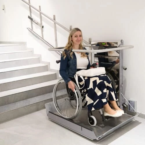 Žena v invalidním vozíku na elektrické plošině pro schodiště.