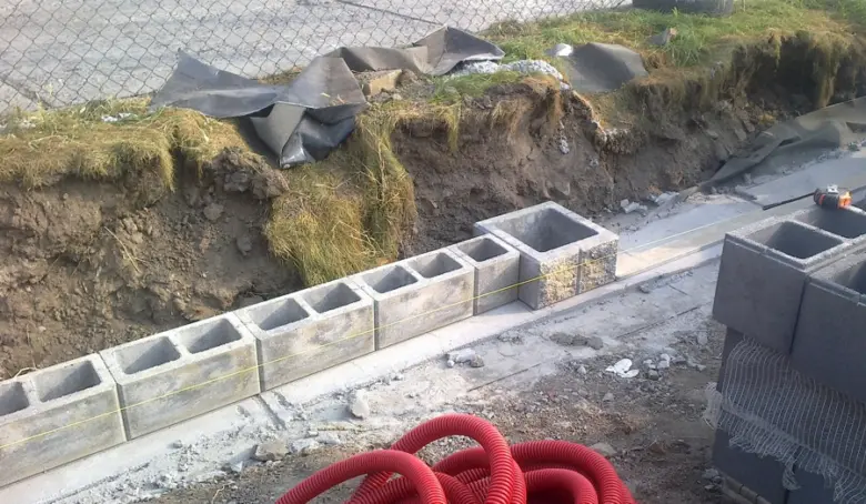 Stavba plotu z betonových tvarnic vedle vykopaného terénu.