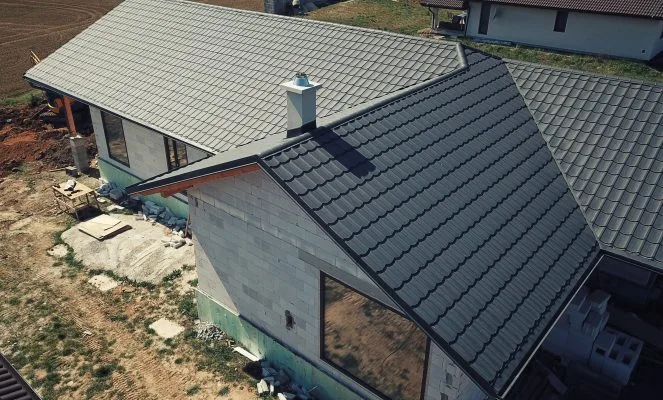 Montáž oplechování střechy s viditelnými závětními lištami na stavbě domu.