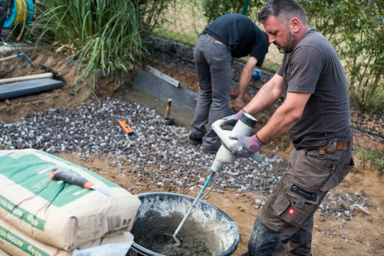Muž míchá beton ručním směšovačem vedle sáčku suché betonu.