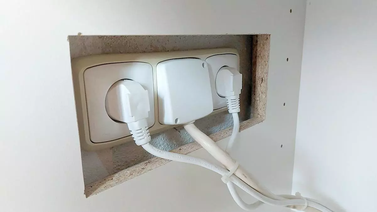 Tři elektrické zásuvky v hrubém otvoru ve zdi s viditelnými kabely.